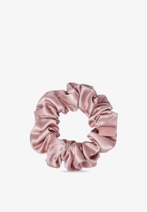 Lichtroze satijnen scrunchie met geplooide stof en een klein rechthoekig merklabel eraan bevestigd.