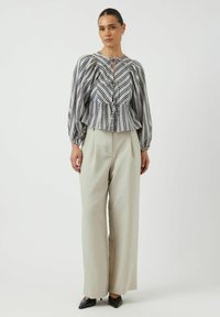 Camicia a scacchi in bianco e nero con maniche a palloncino, vita arricciata e dettaglio a chiave, abbinata a pantaloni larghi a vita alta grigio chiaro.