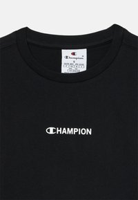 T-shirt noir à col rond avec le logo blanc de Champion centré sur la poitrine et une étiquette de taille indiquant la taille petite pour les âges de 7 à 8 ans.