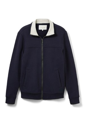 Marineblå zip-jakke med en lys grå krave. Har to sidelommer, ribbede manchetter og en glat tekstur. Rent design uden mønstre.