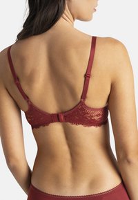 Soutien-gorge en dentelle rouge avec bretelles réglables, délicat motif floral le long du bord, et un système d'attache à crochets au dos. Texture du tissu lisse.