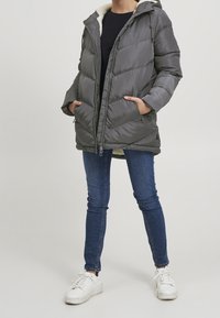 Šedá pufovaná bunda se zipem vpředu, kapucí a kapsami. Obsahuje měkkou bílou fleecovou podšívku a diamantové prošívání. V kombinaci s modrými d�žíny a bílými teniskami.