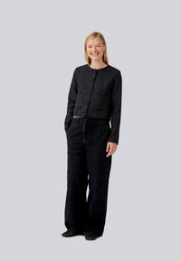 Casaco preto cropped com dois bolsos frontais e botões grandes, combinado com calças pretas de corte largo. Tecido macio e design descontraído.