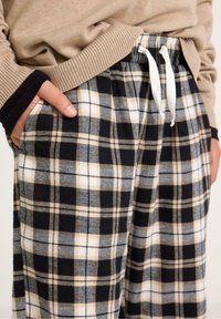 Plaid loungebukser i sort, beige og gråt flannel. Har elastik i taljen med hvid snor og sidelommer.