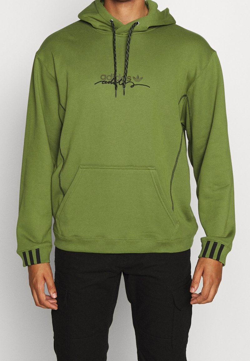 Grön huvtröja av mjukt tyg med en känguruficka. Har en svart logotyp och tre svarta ränder på muddarna.