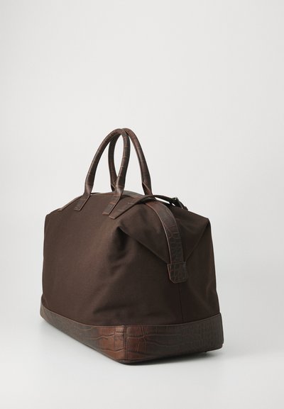 Brown canvas duffel bag with textured brown leather accents, featuring rounded handles and a smooth bottom panel.