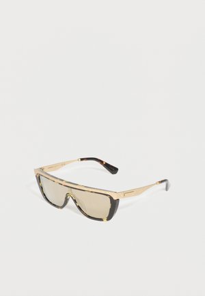 Ochelari de soare cu ramă geometrică aurie și lentile brune colorate, având un design de scut înconjurător și vârfuri ale brațelor de culoare tortoise închisă.