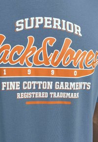 Blauwe katoenen t-shirt met oranje en witte bedrukte tekst: "SUPERIOR Jack & Jones FINE COTTON GARMENTS REGISTERED TRADEMARK."