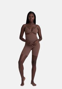 Set di biancheria intima beige senza cuciture composto da un bralette e pantaloni corti fino a metà coscia. Il materiale è liscio e aderente, con spalline regolabili e un design minimalista.