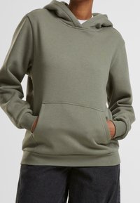 Sweat à capuche vert en tissu doux avec une poche kangourou à l'avant, des poignets et un ourlet côtelés. Doté d'une capuche avec cordon de serrage et d'une coupe décontractée.