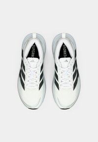 Λευκά αθλητικά παπούτσια με λείο συνθετικό επάνω μέρος, μαύρες ρίγες και μαξιλαρωμένη σόλα. Τα κορδόνια είναι λευκά και το εσωτερικό φέρει την επωνυμία «SUPERNOVA».