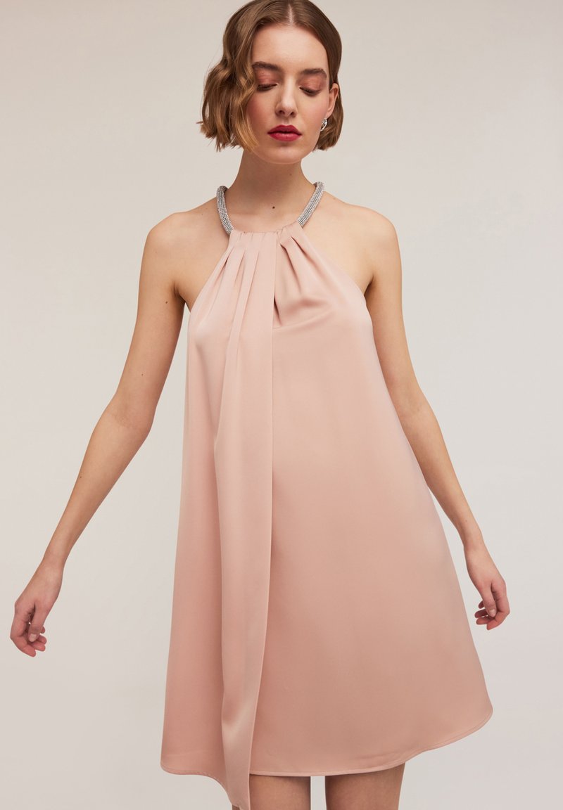 Rochie cu gât halter dintr-un material roz moale, cu pliseuri și accente de mărgele transparente la decolteu. Fără mâneci, cu o formă A-line relaxată.