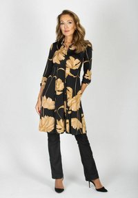 Czarna sukienka z beżowym kwiecistym wzorem, z zapinaniem na guziki z przodu, z rękawami o długości trzech kwart, w połączeniu z czarnymi spodniami i czarnymi szpilkami. Gładka tekstura.