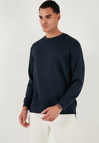 Felpa blu navy con scollo rotondo e maniche lunghe. Texture liscia, dettaglio del logo discreto sul petto, polsini e orlo a costine.