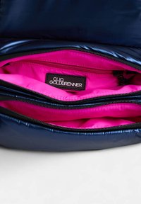 Sac en tissu bleu marine brillant avec un intérieur rose vif. Il possède un compartiment zippé et une étiquette noire avec "CLIO GOLDBRENNER."