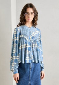 Blå mønstrete skjorte med hvite geometriske design, lange ermer og rund krage; paret med et dongeri skjørt.