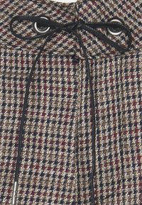 Vävt tyg med ett rutmönster i brunt, marinblått och rött, med svarta dragsnören och metallöglor i midjan.