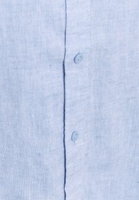 Tessuto di lino blu chiaro con due piccoli bottoni abbinati allineati verticalmente lungo una patta di bottonatura cucita.