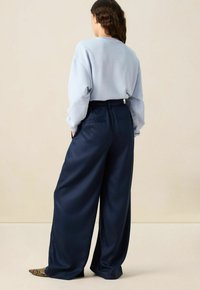 Wijdvallende marineblauwe broek van gladde stof, met een hoge taille en zijzakken, gecombineerd met een lichtblauwe sweatshirt.