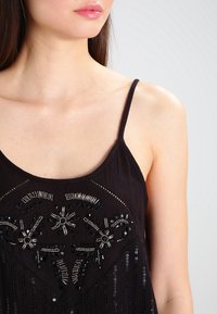 Haut sans manches noir avec des embellissements en perles complexes, des sequins et une texture douce, conçu avec une silhouette fluide.