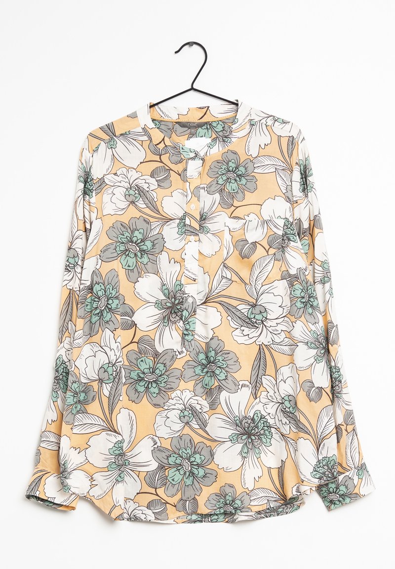 Blouse à manches longues à fleurs avec un fond pêche, des fleurs blanches et bleu sarcelle, boutonnée sur le devant, suspendue à un cintre noir sur un fond blanc.