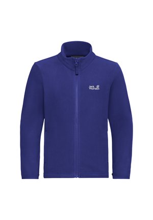 Due bambini che indossano giacche blu Jack Wolfskin con zip e pantaloni beige stanno fianco a fianco su uno sfondo uniforme.