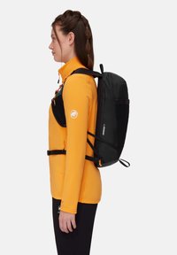 Schwarzer Rucksack mit verstellbaren Riemen, einer strukturierten Oberfläche und orangefarbenen Akzenten, getragen über einer leuchtend orangefarbenen Jacke. Seitenansicht.