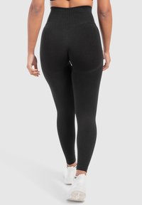 Zwarte high-waisted leggings met een gladde textuur, een nauwsluitend ontwerp en een versterkte tailleband. Gecombineerd met witte sport schoenen.