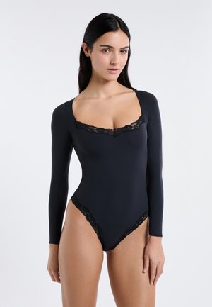 Body noir à manches longues avec un bord en dentelle le long de l'encolure et des ouvertures des jambes, une texture lisse et une silhouette ajustée.