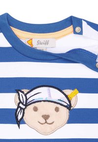 Blå och vit randig skjorta med broderad björns ansikte och bandana. Inkluderar tryckknappar vid axeln för enkel påklädning.