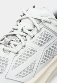 Hvit atletisk sko med mesh-design, syntetiske overlegg, slank form og reflekterende detaljer, samt strukturerte lisser.