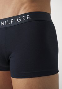 Boxers en coton bleu marine avec une ceinture tonale arborant le logo "HILFIGER" en blanc. Texture lisse, design ajusté, jambes courtes.