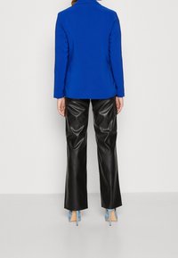 Blå kavaj med snibbkrage, kombinerad med svarta läderbyxor i cargo-stil med sidofickor och ljusblå klackar med spetsiga tår.