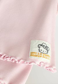 Różowy materiał z rowkami z falbaniastym dołem oraz metką z wzorem Hello Kitty i napisem "HELLO KITTY."