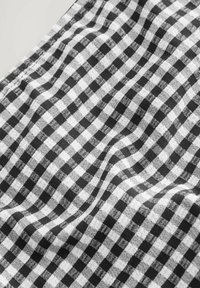 Svart och vit gingham bomullstyg med ett rutmönster av jämnt fördelade rutor, mjuk textur och en lätt drapering.