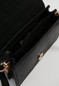 Černá kožená crossbody taška má hladkou texturu, zlaté kovové detaily a několik vnitřních přihrádek, včetně kapsy na zip.