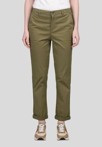 Chinos vert olive avec une coupe droite, fabriqués en coton, dotés de bas de pantalon retroussés et d'une fermeture à bouton, associés à des baskets beiges.