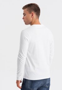 Weißes Langarmshirt mit Rundhalsausschnitt, aus Baumwolle, mit glatter Textur und taillierter Silhouette, kombiniert mit blauen Jeans.