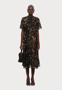 Vestito a fantasia floreale nero e oro con maniche a sbuffo corte e vita cinchata, abbinato a una borsa nera e sandali con cinturini.