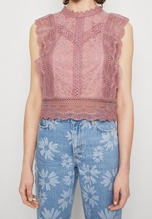 Mouwloze roze kanten top met geschulpte randen gecombineerd met een high-waist blauwe jeans met grote witte bloemenprints.