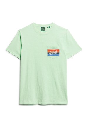 Camiseta de algodón de manga corta en verde claro. Presenta un bolsillo en el pecho izquierdo con una etiqueta gráfica multicolor. Textura suave.