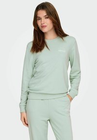 Lys grøn genser med rund hals og ribbestrikkede mansjetter. Har «LIMITLESS» i hvit tekst på brystet. Laget av mykt materiale.