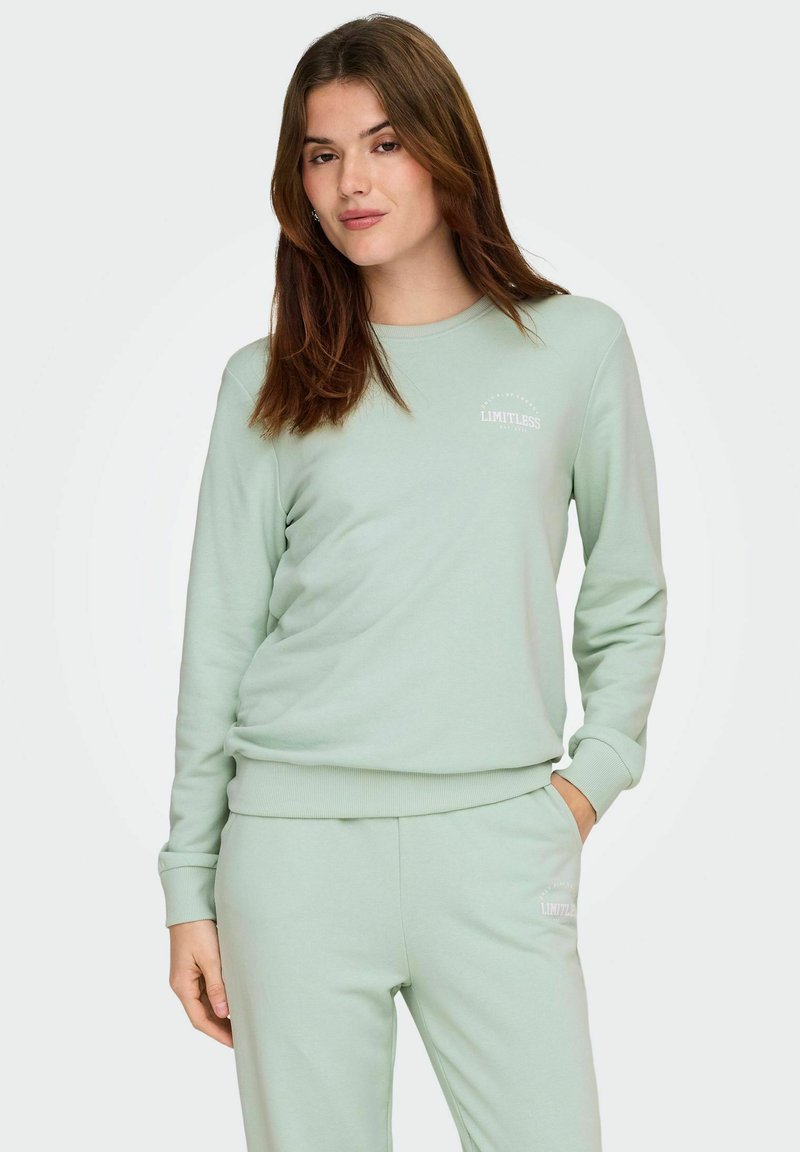 Lys grøn genser med rund hals og ribbestrikkede mansjetter. Har «LIMITLESS» i hvit tekst på brystet. Laget av mykt materiale.