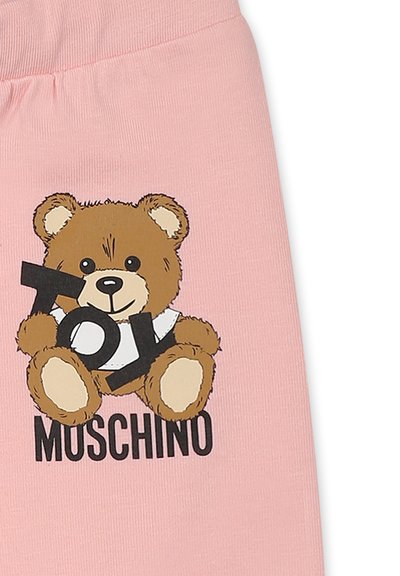 Roze katoenen kledingstuk met een cartoonbeer die een zwart "TOY"-bord vasthoudt, met daaronder de tekst "MOSCHINO" in het zwart.