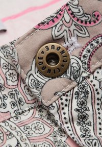 Katoenen stof met ingewikkeld paisleyprint in crème, roze en zwart. Heeft een messing knoop en witte stikdetails.