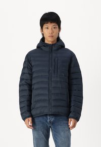 Mørkeblå polstret jakke med glidelås foran, fast hette og brystlomme. Har kviltet tekstur og elastiske ermer.