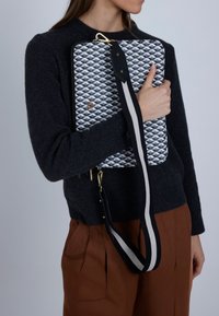 Texturerad rektangulär väska med ett blått och vitt geometriskt mönster, svart rem med vit rand, guldfärgade detaljer och dragkedjestängning.