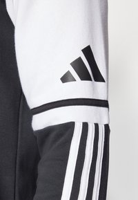 Zwart-wit sportieve sweatshirt met een textuurafwerking, opvallende witte strepen en een zwart Adidas-logo op de bovenste mouw.