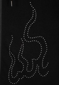 Chaqueta negra con cremallera, que presenta un diseño ondulado hecho de pequeños rhinestones plateados. La tela tiene una textura suave y una silueta ajustada.