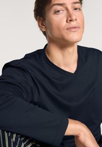 Marineblauwe langarm V-hals shirt gemaakt van zacht materiaal, met een gladde textuur. Geplaatst op een neutrale achtergrond, die de kleur van de stof accentueert.
